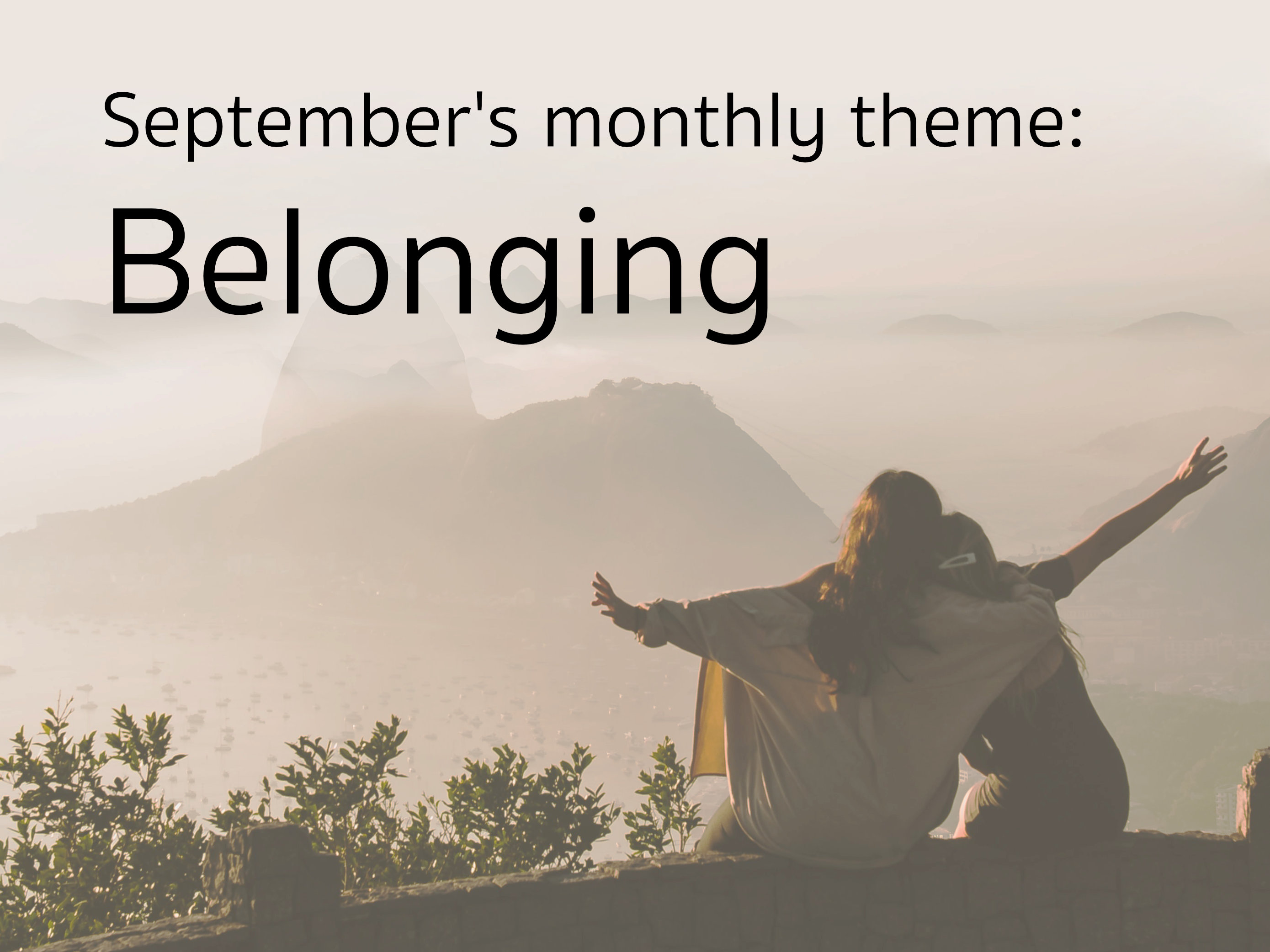 image of two people sitting together overlooking a foggy gorge. Text says September's monthly theme: Belonging